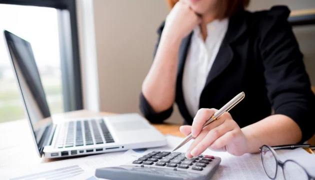 Бухгалтерка проводить розрахунки з калькулятором та ноутбуком в офісі
