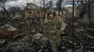 Український військовий у камуфляжі проходить через зруйноване село під час війни