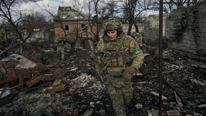 Український військовий у камуфляжі проходить через зруйноване село під час війни