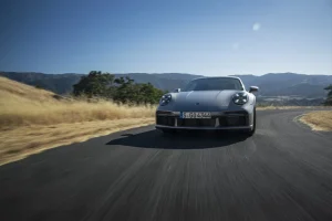 Porsche 911 мчить звивистою дорогою серед пагорбів під сонцем