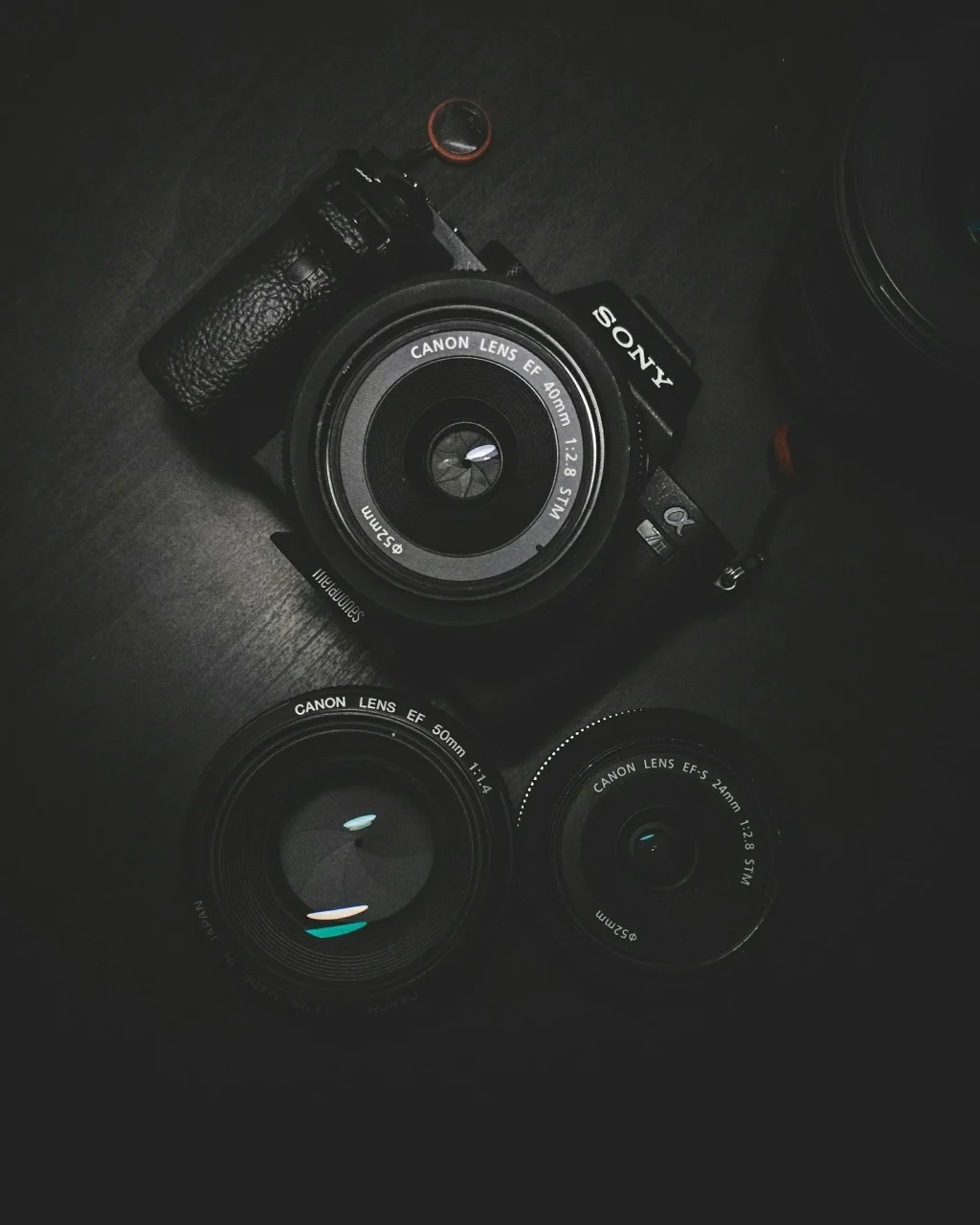 Чорна камера Sony з трьома обєктивами Canon на темному столі