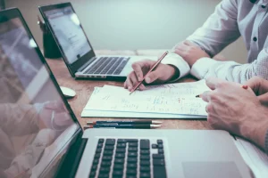 Руки бізнесменів за деревяним столом з ноутбуками та документами зі схемами