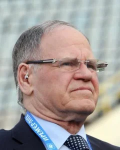 Йожеф Сабо в окулярах з навушником та бейджем Премєр-ліги на тлі стадіону