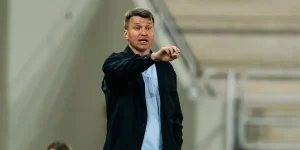 Руслан Ротань у темній куртці вказує рукою на стадіоні