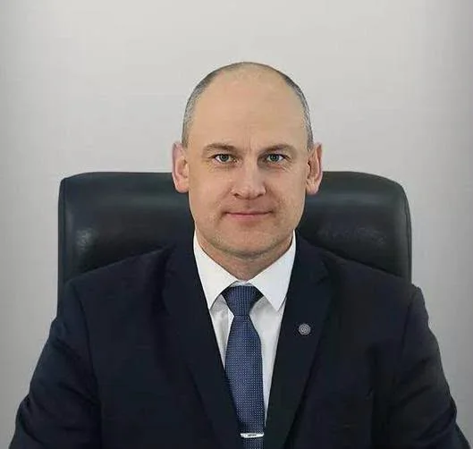 Чоловік у темному костюмі з блакитною краваткою сидить у чорному кріслі